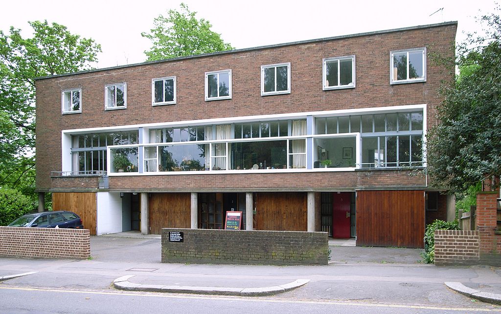 A two-story modern brick building with large windows, five garage doors on the ground floor, and a small sign in front. Trees and a parked car are visible. | Steve Cadman from London, U.K., CC BY-SA 2.0, via Wikimedia Commons