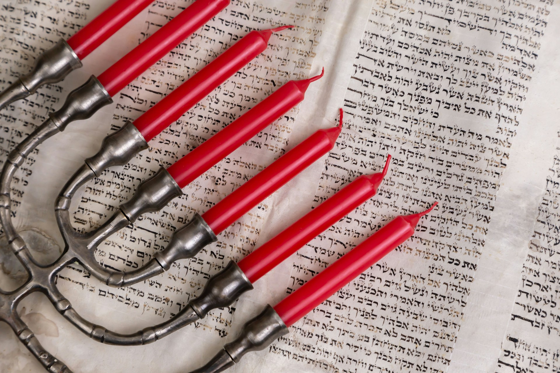 A menorah with red candles on a Hebrew text document. | Photo by Diana Polekhina on Unsplash