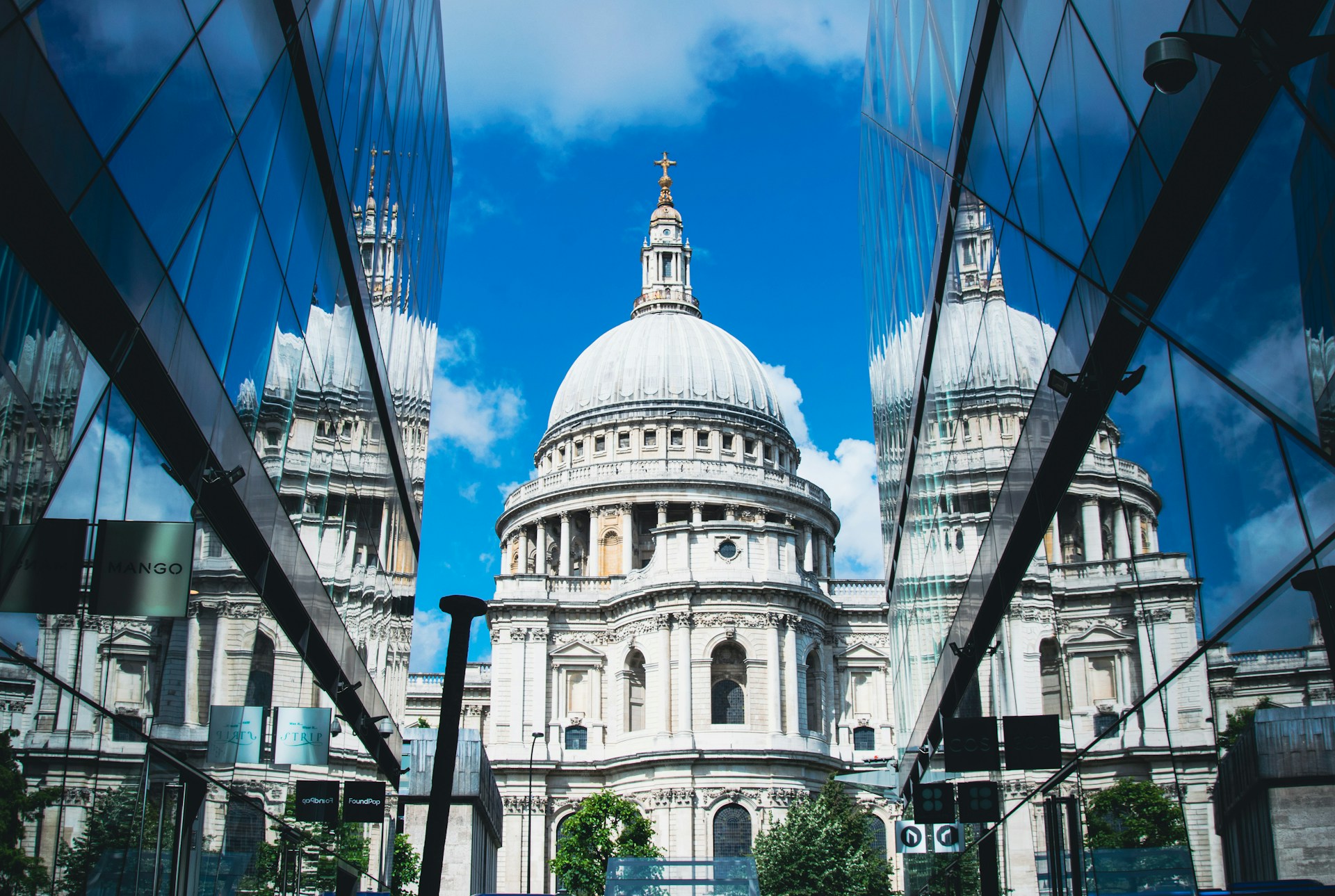 St. Paul's Cathedral framed by modern glass buildings under blue sky. | Photo by Robert Stump on Unsplash
