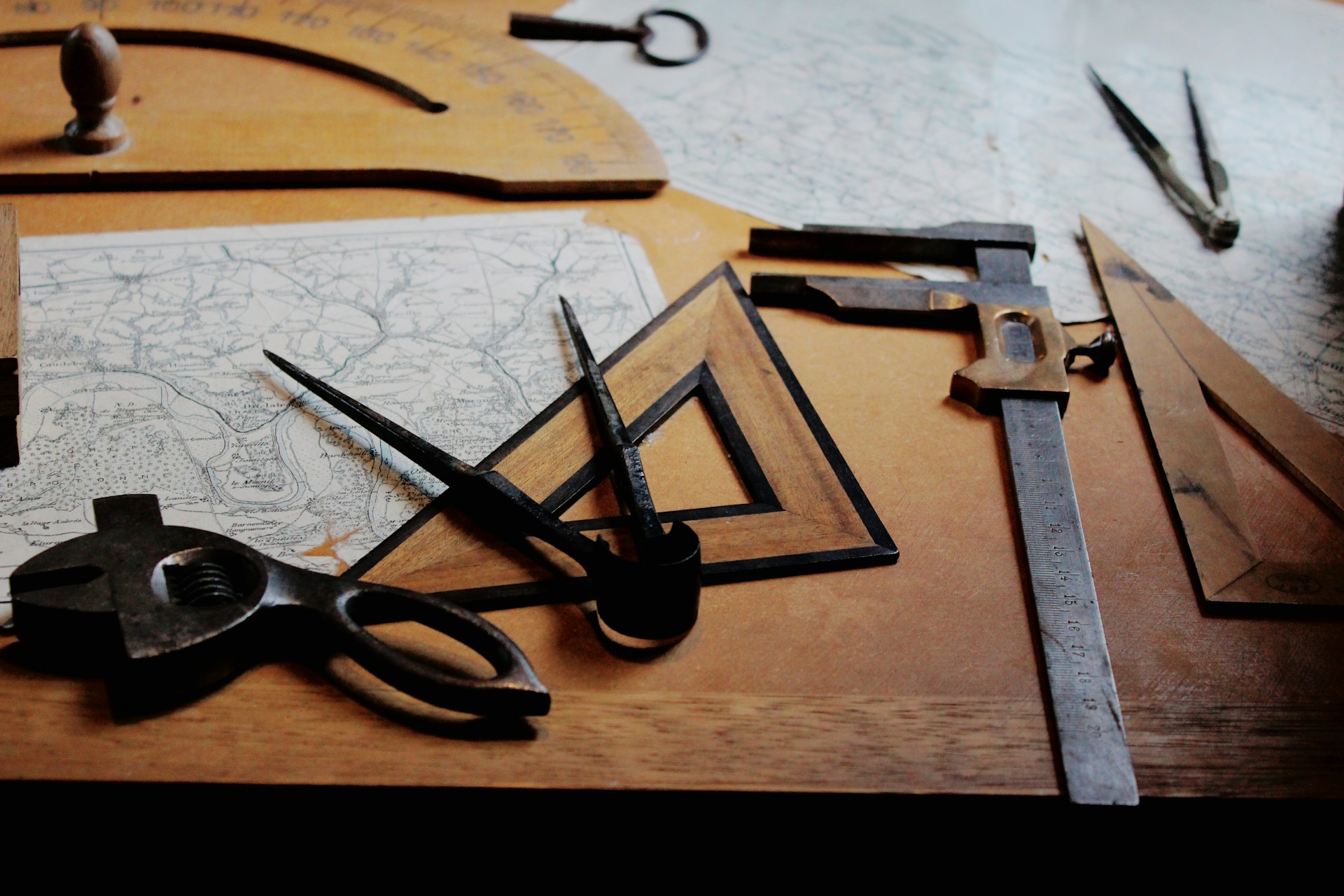 Old drafting tools on a desk with a map and wooden drawing board in the background. | Photo by Fleur on Unsplash