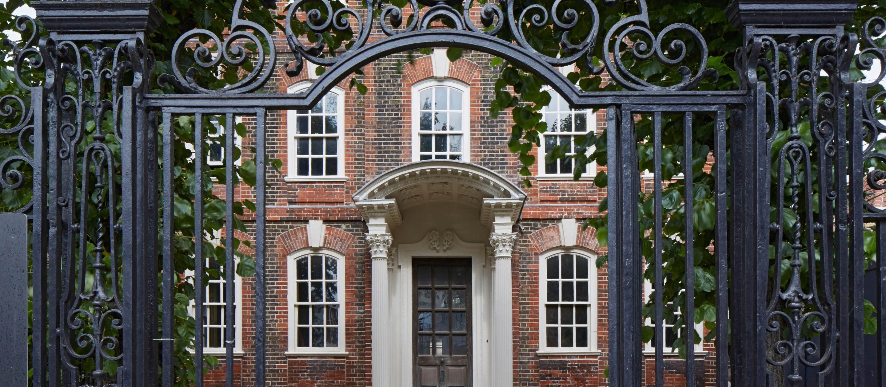 Ornate iron gate opening to a classic brick building with white-trimmed windows and door. | National Trust Images/Dennis Gilbert. The entrance at Rainham Hall