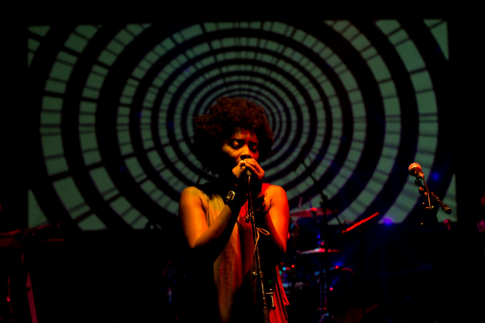 A musician on stage with a backdrop of concentric circles and stage equipment. | Photo by Kobe Subramaniam on Unsplash