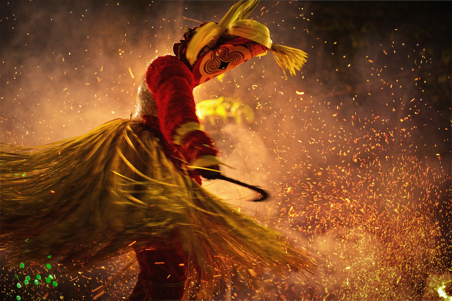 Dancer in ornate costume amidst sparks at a cultural festival at night. | Photo by Manyu Varma on Unsplash