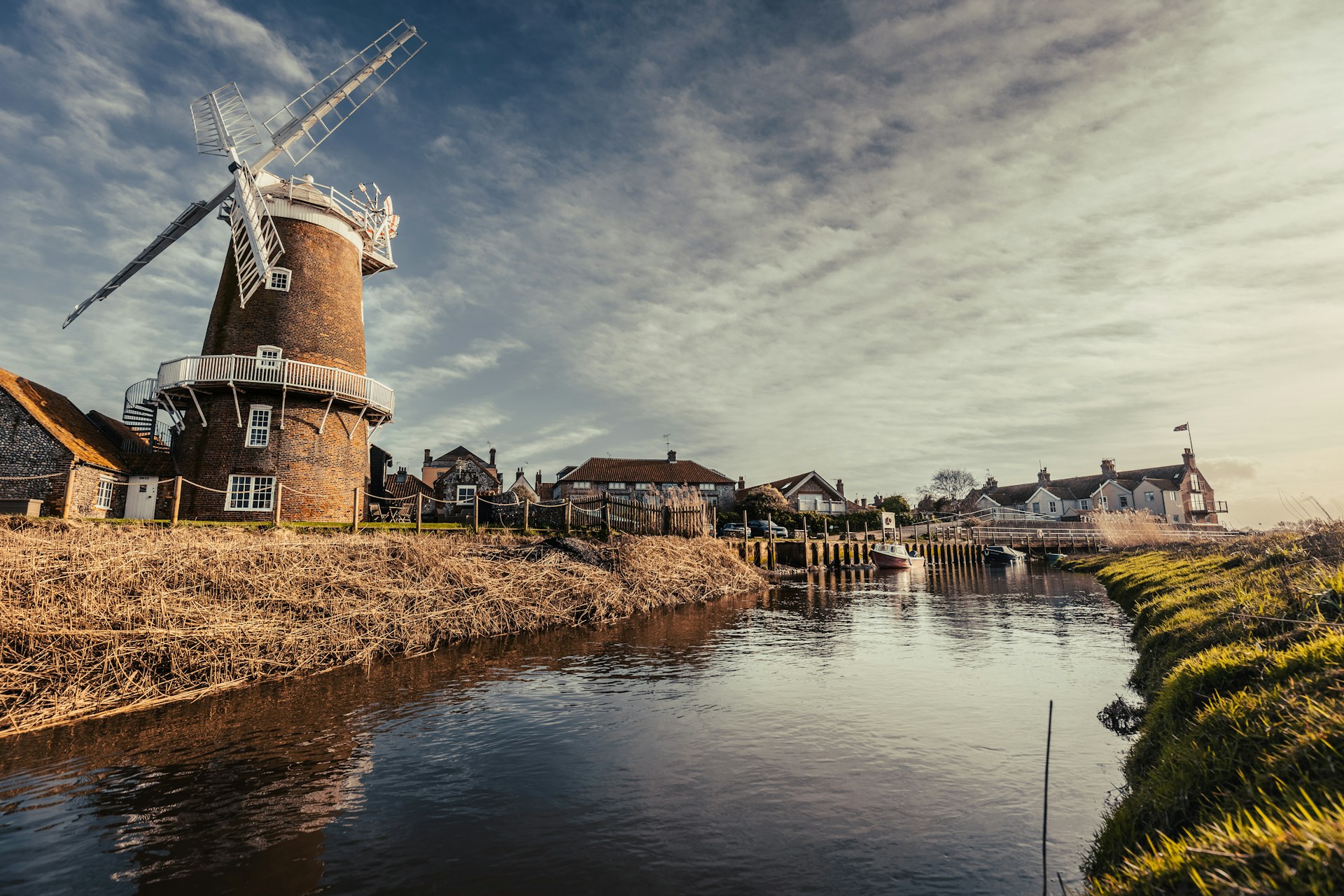 Traditional windmill by a river with houses and a clear sky in the background. | Photo by Ben Wicks on Unsplash