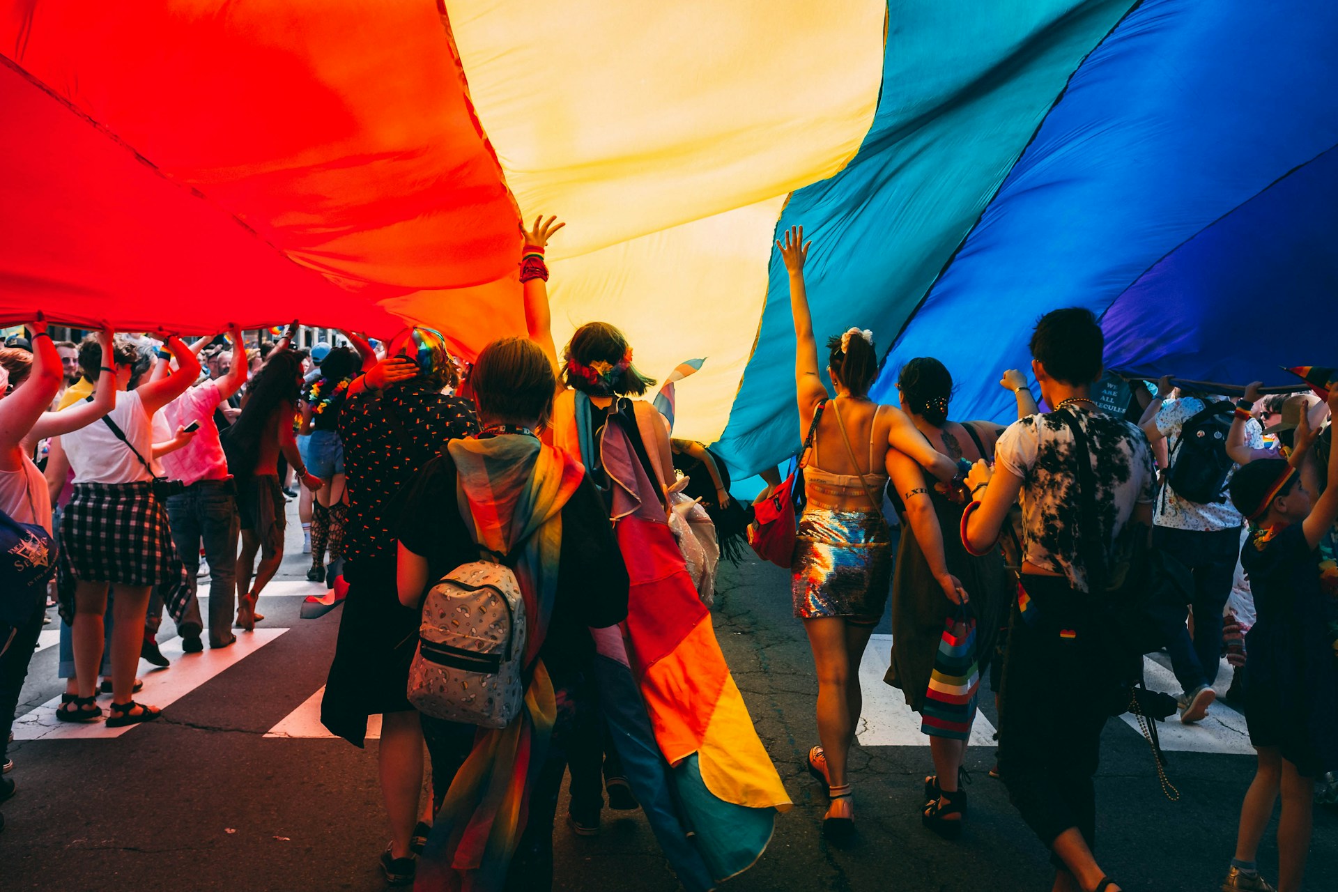 Crowd of people marching under a large rainbow flag at a pride parade. | Photo by Mercedes Mehling on Unsplash