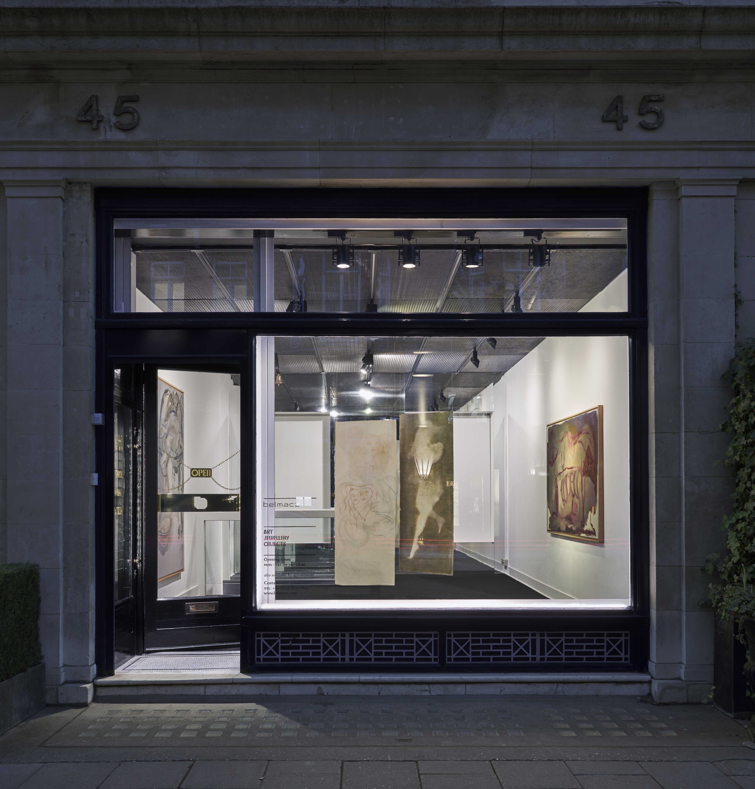 Art gallery storefront at night with visible interior and displayed artwork. | Belmacz