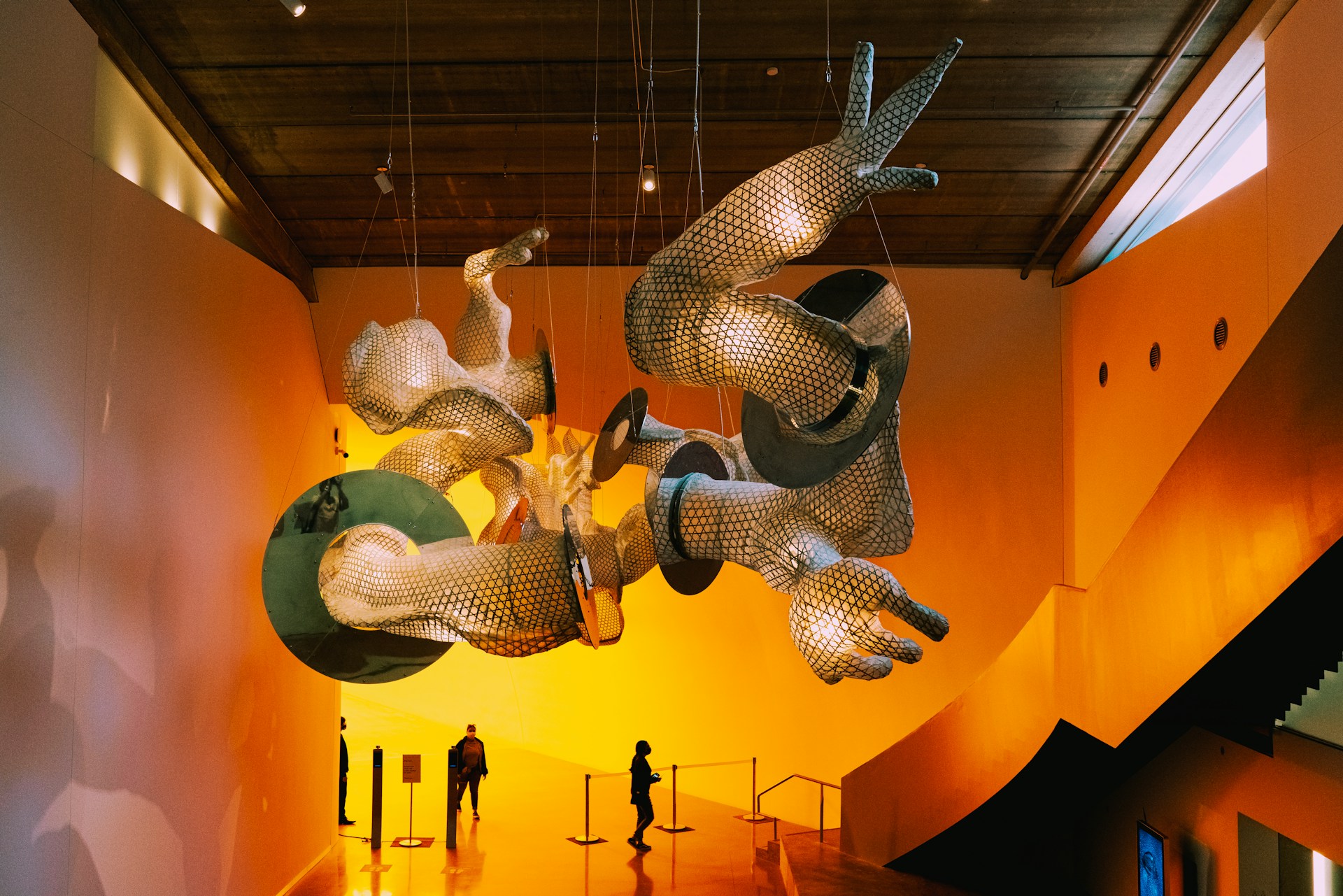 Art installation with large mesh sculptures hanging above gallery visitors in a warm-lit room. | Photo by Adrian Newell on Unsplash