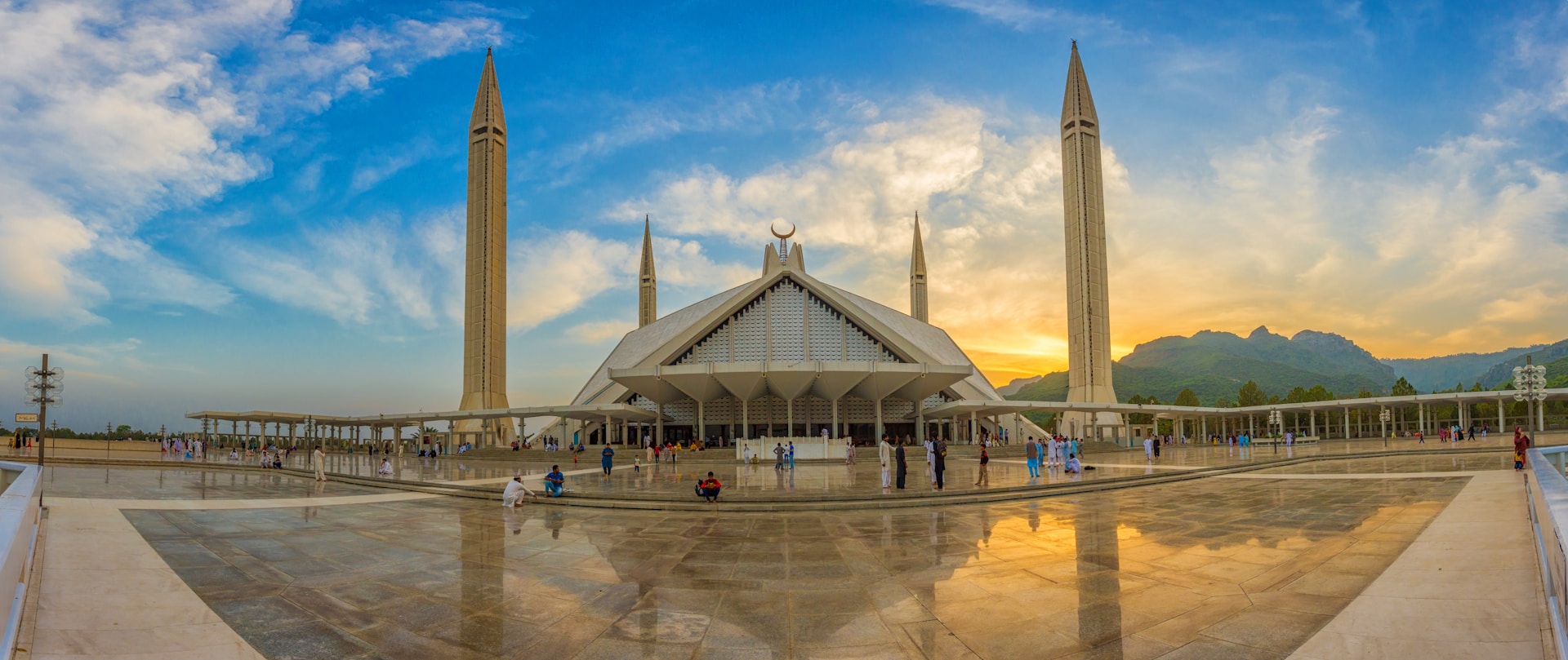 Panoramic view of a modern mosque with towering minarets and visitors at sunset. | Photo by Syed Bilal Javaid on Unsplash