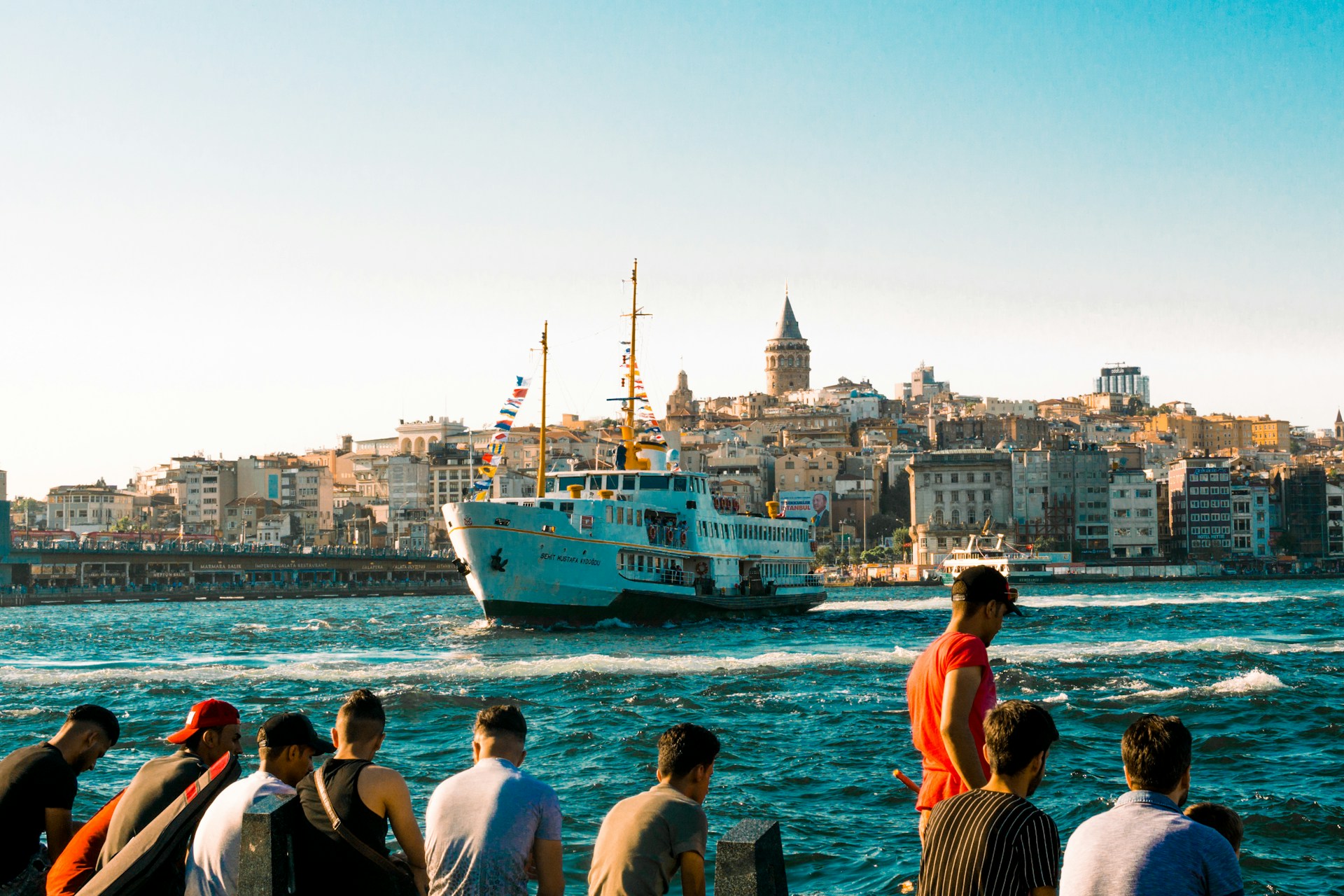 A ferry in a bustling harbor with a historical city skyline in the background. | Photo by Meriç Dağlı on Unsplash
