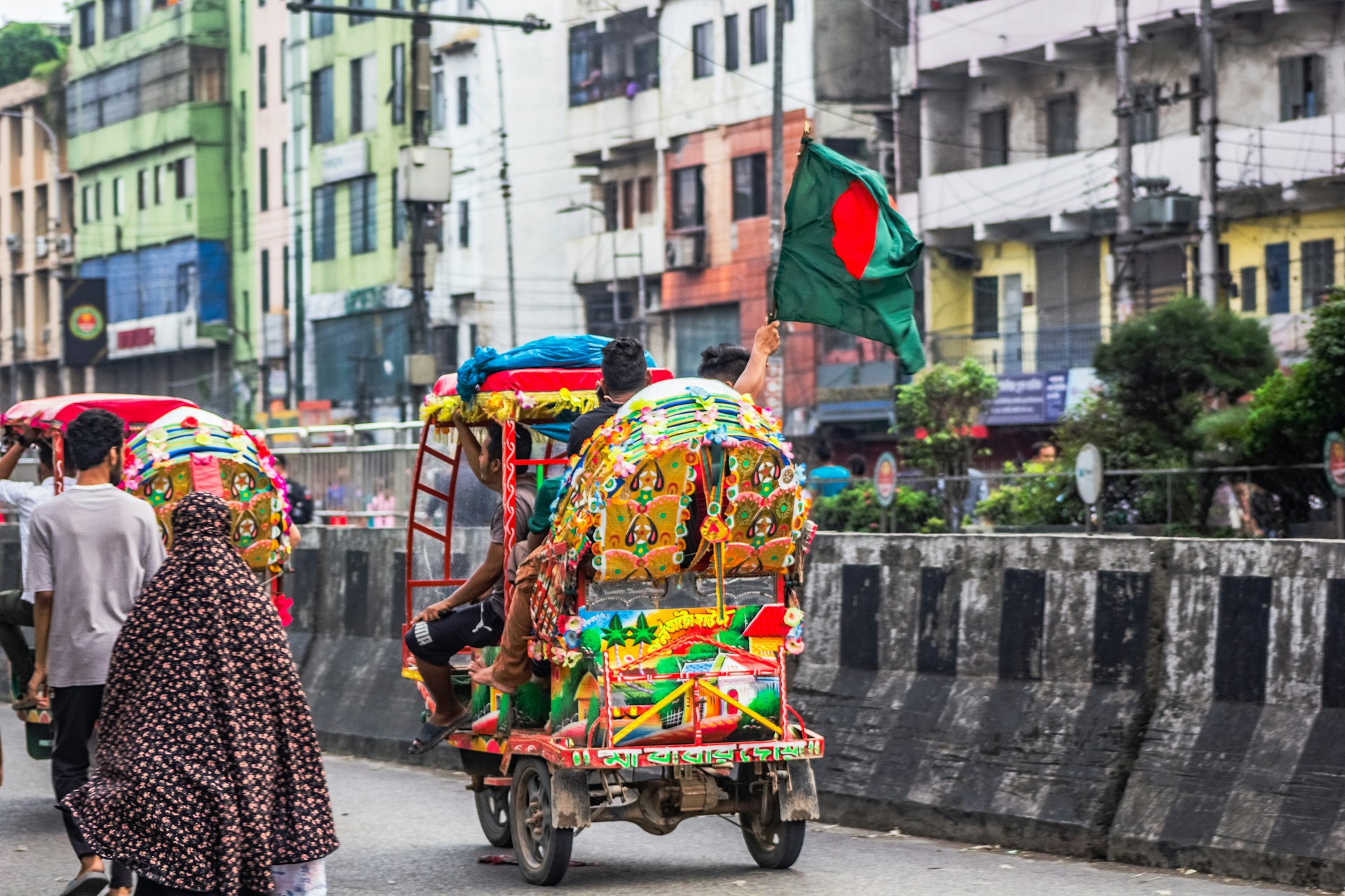 Colorful rickshaws on a city street with a person waving a flag. | Photo by Bornil Amin on Unsplash