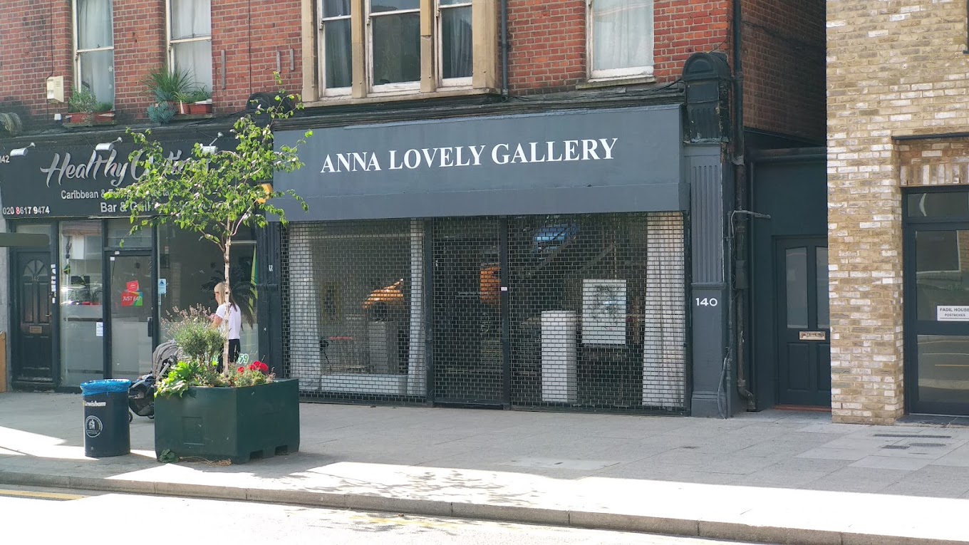 Exterior of the 'ANNA LOVELY GALLERY' with a dark facade, next to a planter and trash bins. | 2024 Anna Lovely Gallery