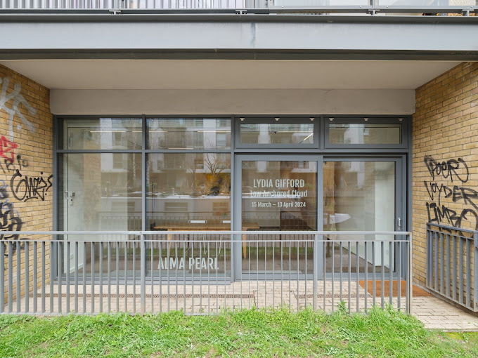 Exterior of a gallery with signage for a Lydia Gifford exhibit, graffiti on brick walls, and a metal railing. | Alma Pearl