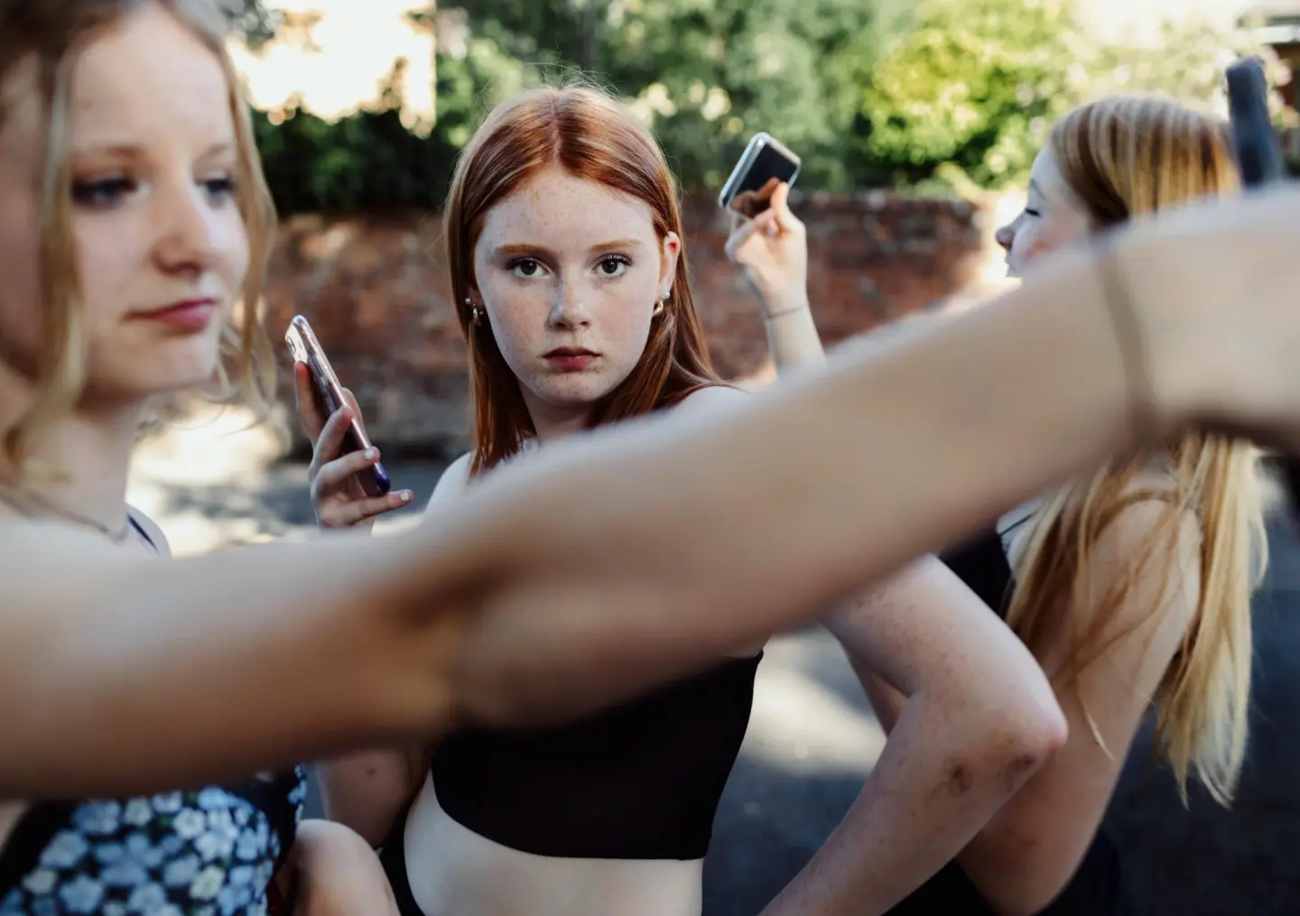 Three people using smartphones, one capturing a selfie, outdoors.