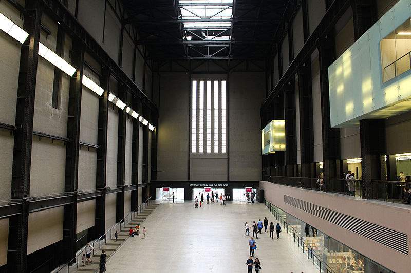 Interior of a spacious industrial-style hall with people and high ceilings.