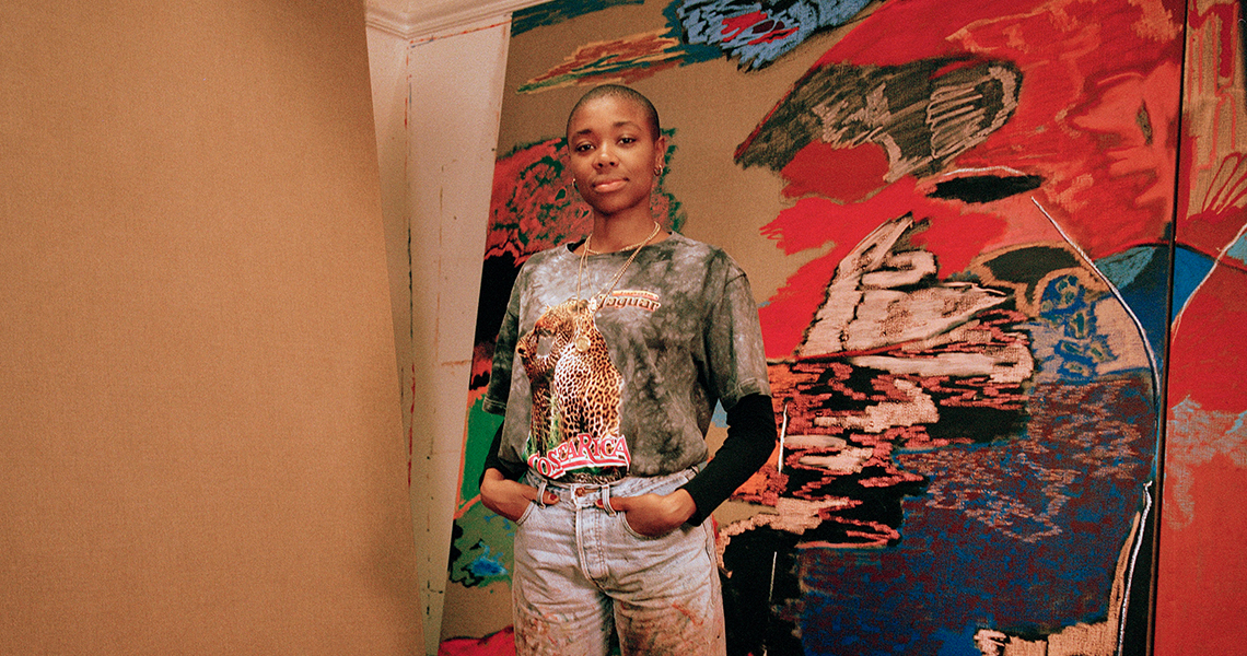Person standing in front of a vibrant abstract painting, wearing a tie-dye shirt and jeans.