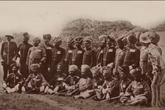 Vintage photo of a group of uniformed soldiers standing and sitting outdoors.
