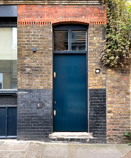 A tall dark blue door set in a brick wall with a semicircular arch above it. | 2024, A.I. Gallery