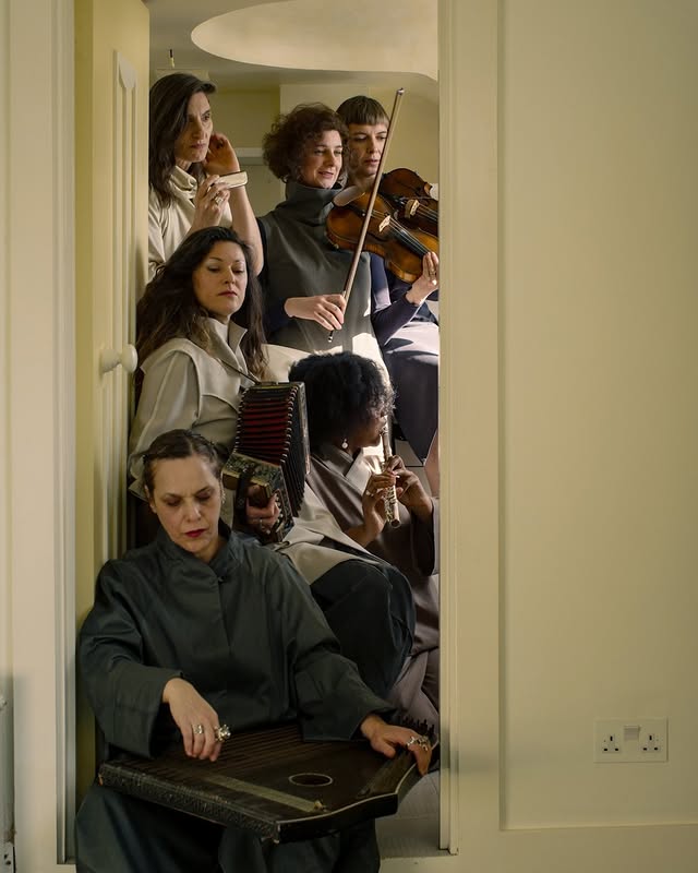 A group of musicians in muted clothing play various instruments, gathered in a narrow doorway, creating an intimate musical atmosphere.