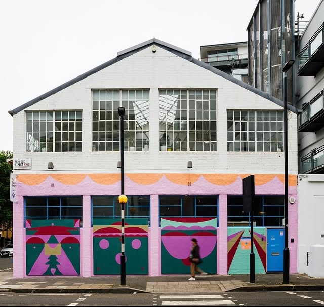 A colorful, mural-adorned building with large windows, featuring geometric designs, is framed by a pedestrian walking by.