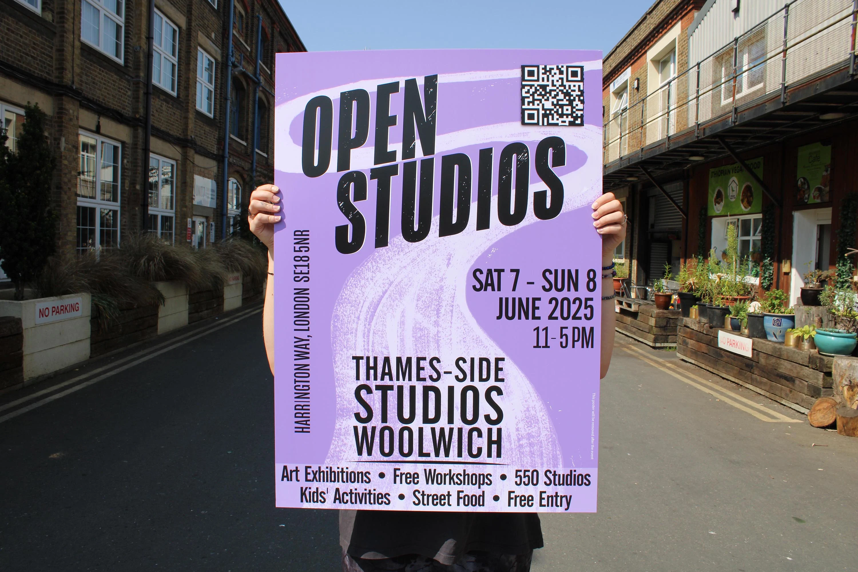 A person holds a vibrant poster advertising the Open Studios event at Thames-Side Studios, Woolwich, on June 7-8, 2025.