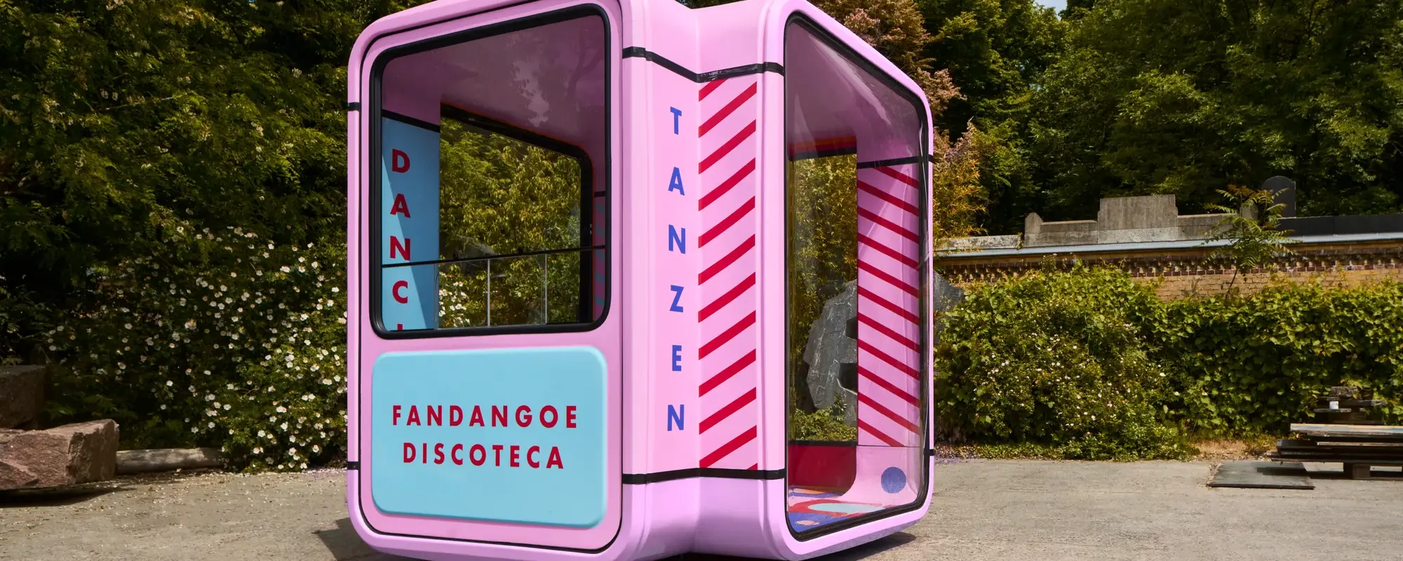 A colorful, modern booth labeled “Fandangoe Discoteca” with playful stripes, set against a lush green backdrop.