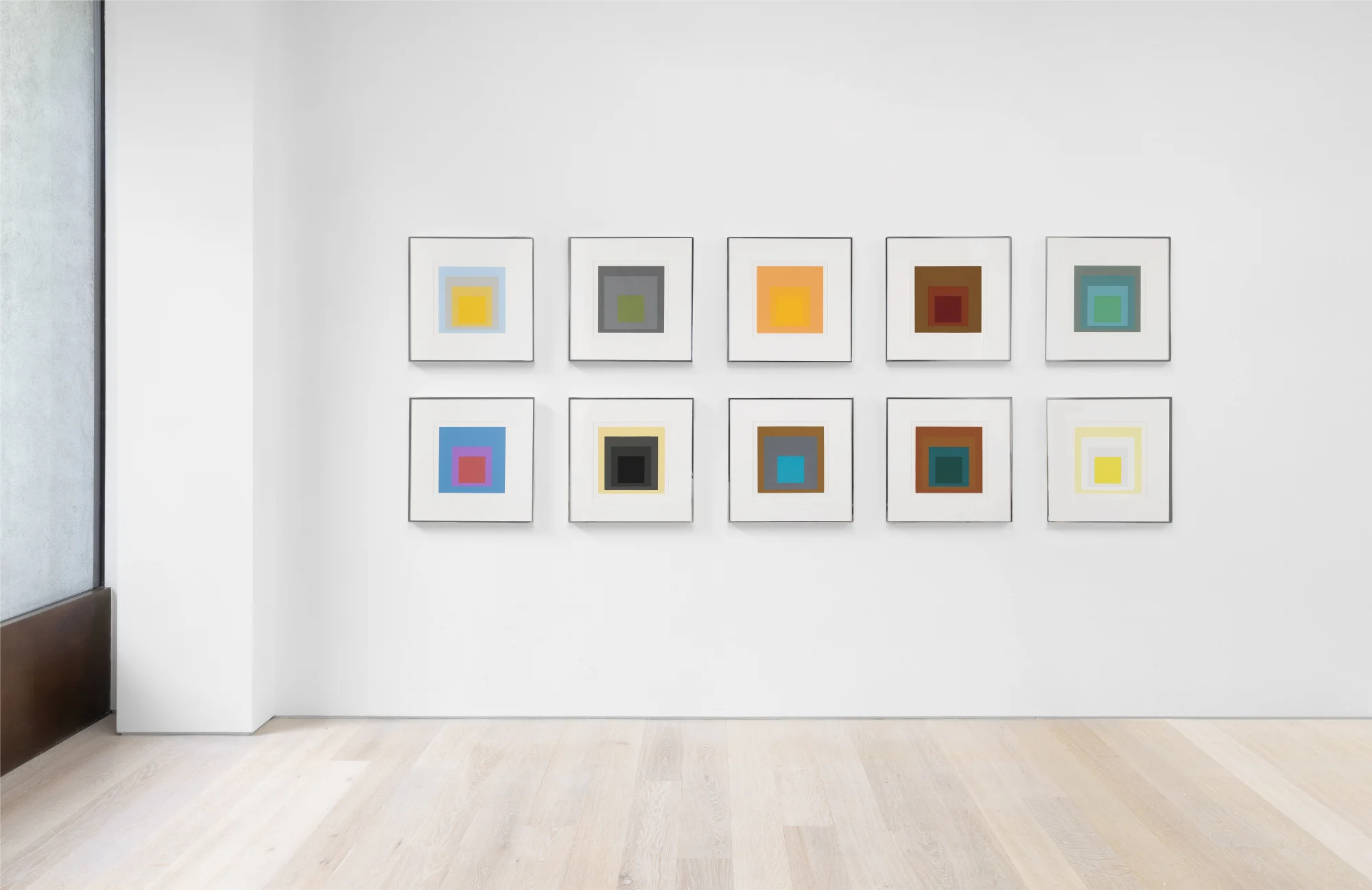 A gallery wall featuring nine framed geometric color block artworks arranged in three rows, set against a white background.