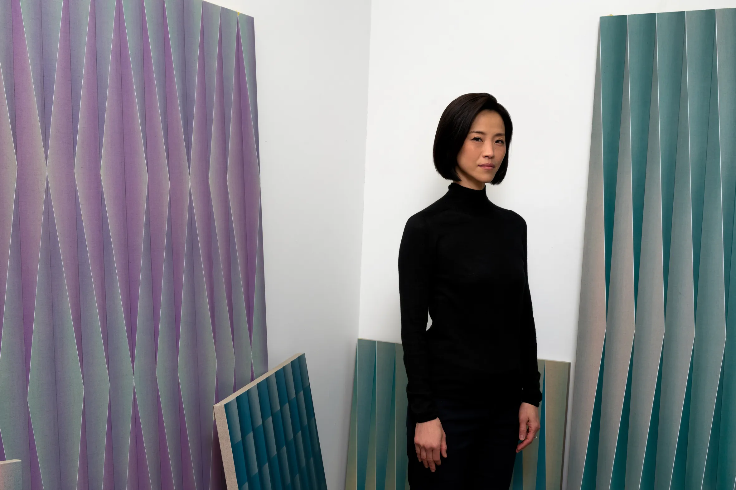 A person stands against a white wall, flanked by colorful, textured panels in shades of purple and teal, creating a modern aesthetic.