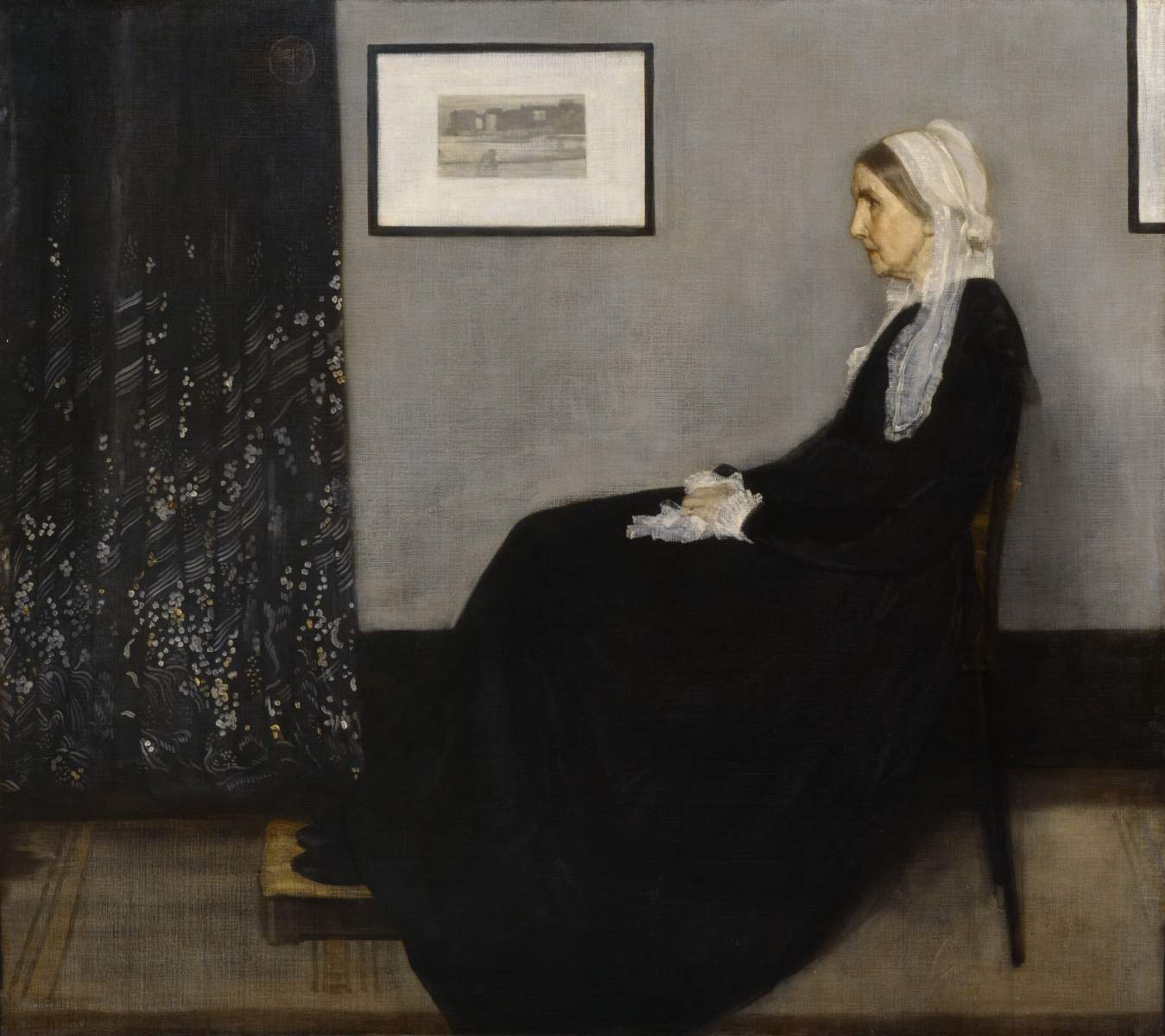 Portrait of a seated woman in a dark dress, with a light-colored head covering, in a room with a dark patterned curtain and a framed picture.