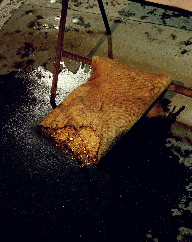 A burlap sack filled with debris sits on a wet, dark surface next to a metal stand.