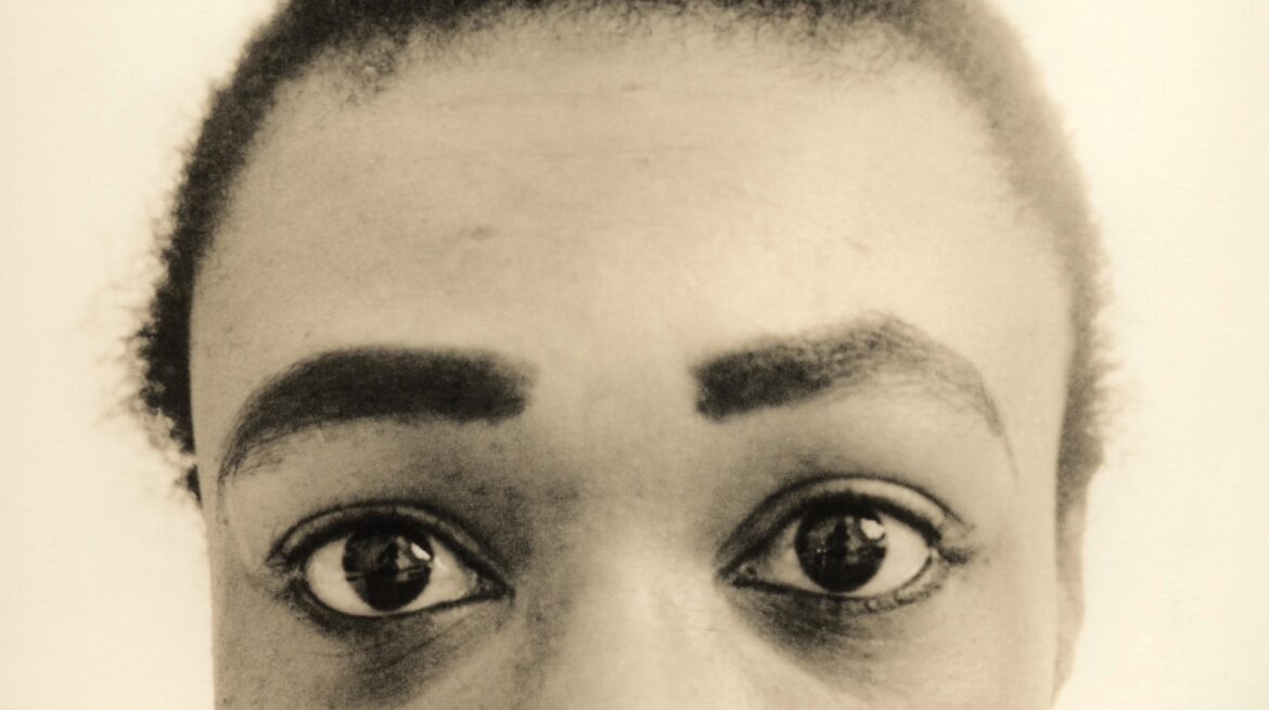A close-up of a person's eyes, showcasing their eyelashes and eyebrows. The image is in black and white, with a focus on the human face, including the forehead.