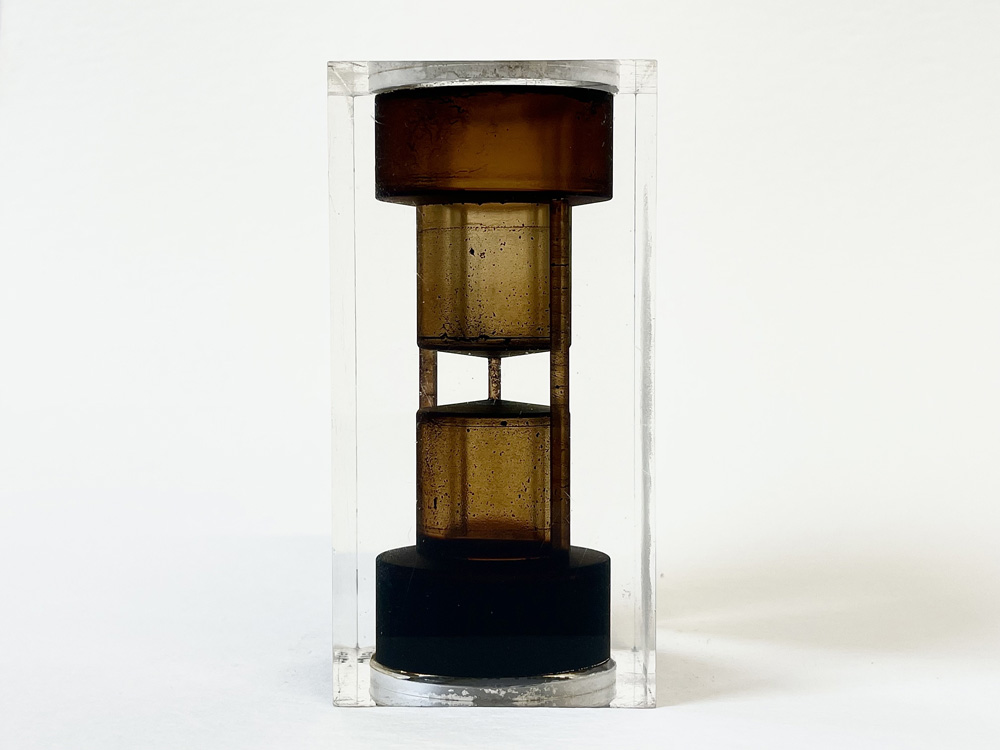 A clear cylinder encases a layered, brown hourglass with a black base, showcasing a unique and modern design.