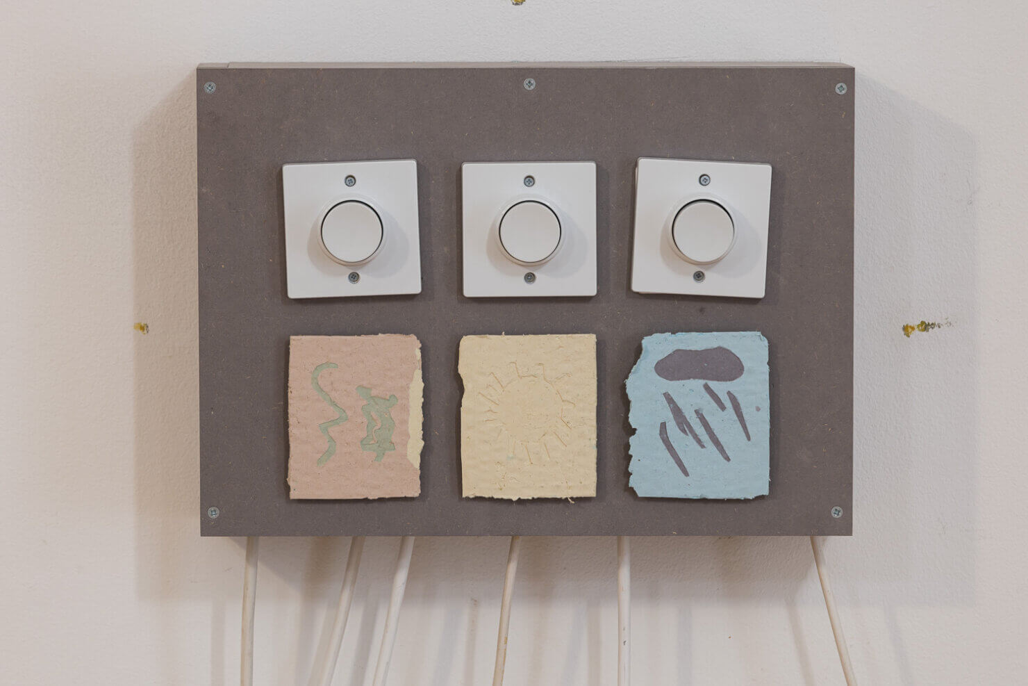 A control panel featuring three circular knobs above textured, colored squares representing weather: lightning, sun, and rain.