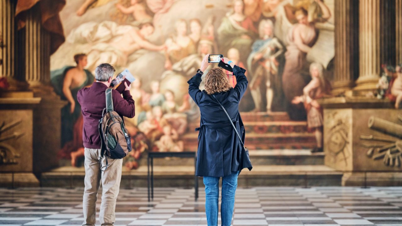 A couple of people standing in front of a painting, taking pictures with their smartphones. The woman is wearing casual clothing and footwear while focusing on the artwork.