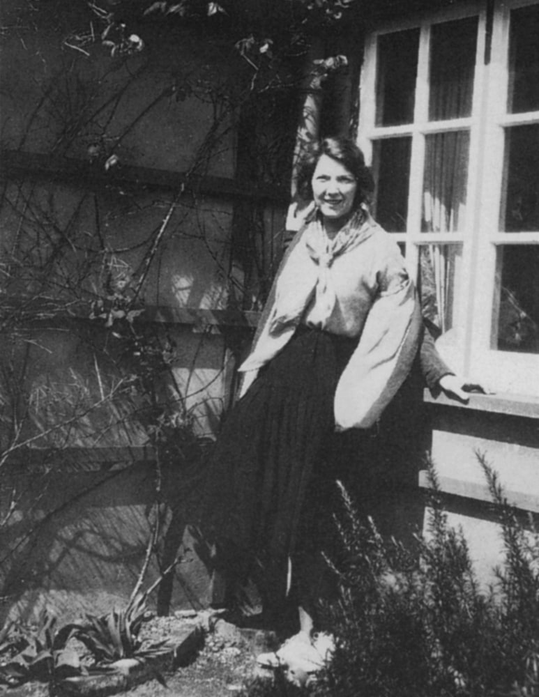 A woman with dark hair is leaning against a window, looking outside. The image is in black and white and features a building in the background.