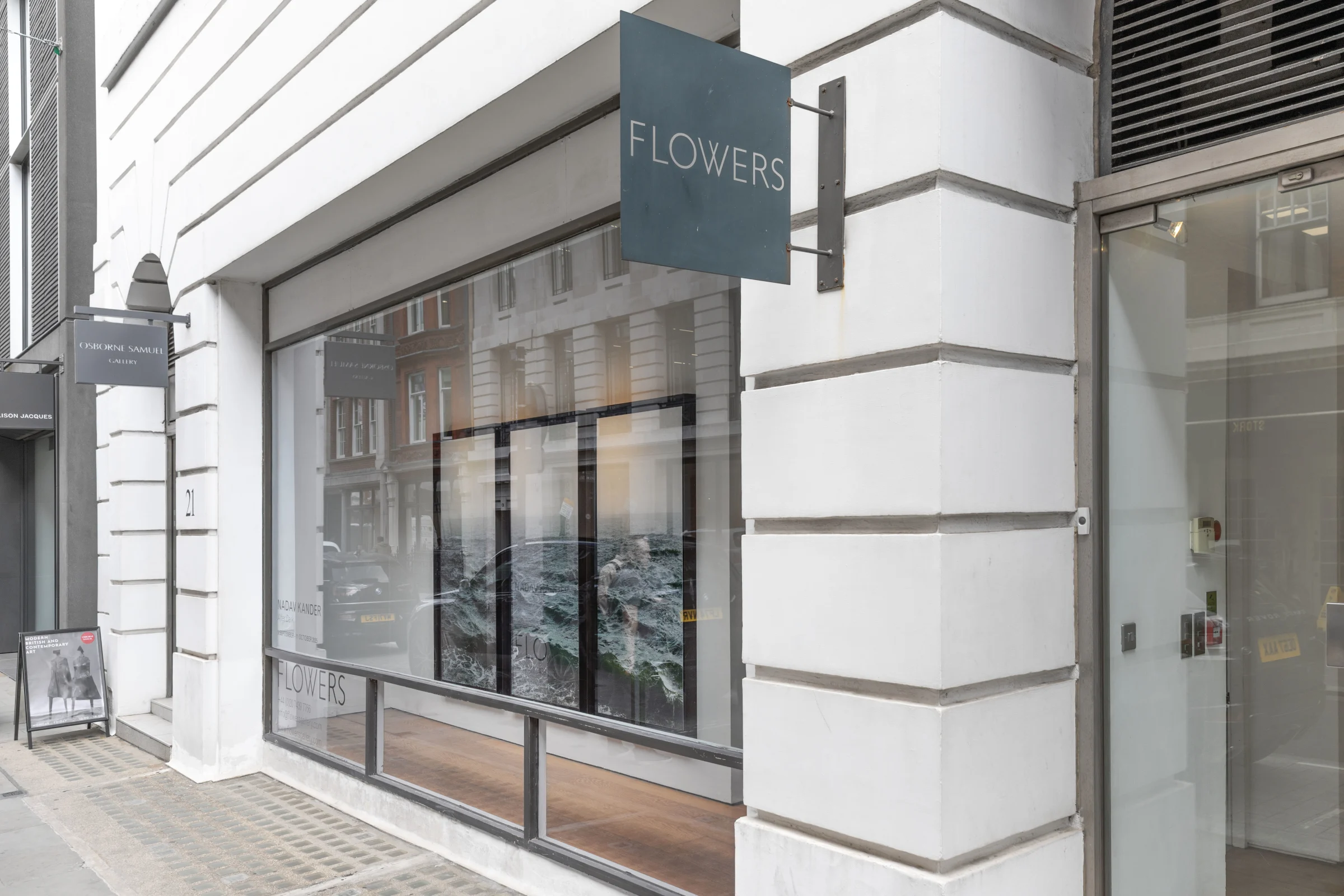 A storefront featuring a sign on the front that reads Flowers, with visible doors and windows. The building is situated along a street with a sidewalk in front, showcasing architectural details.