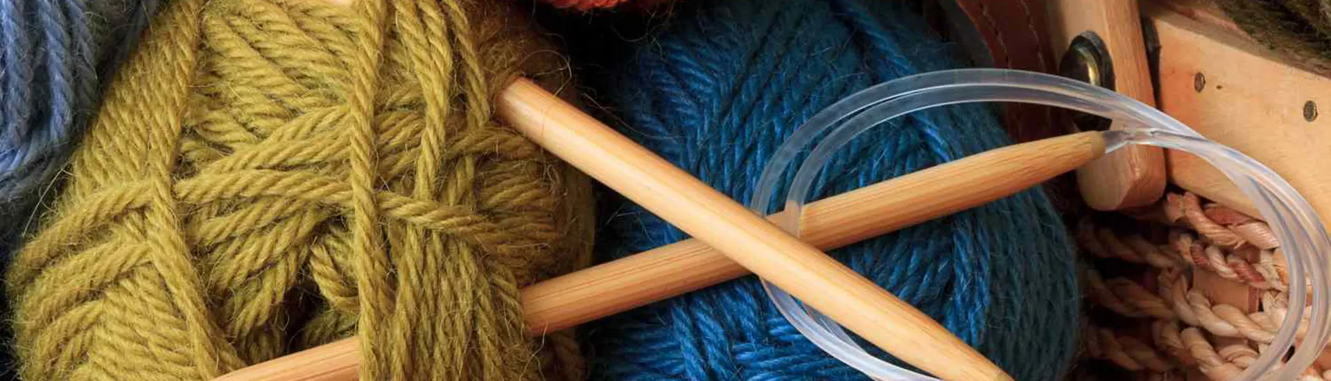 A close-up of colorful yarn threads, highlighting their texture and fibers, with a needle placed nearby, set against an indoor background.