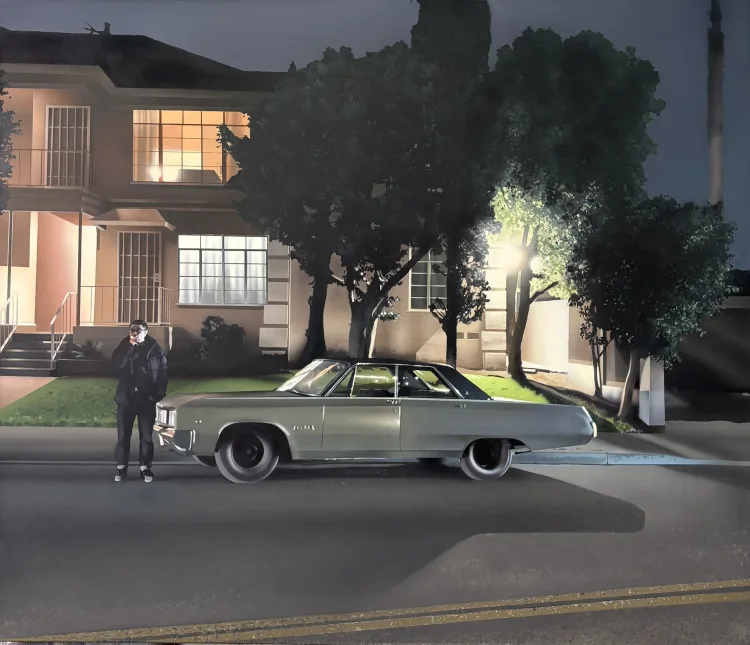 A man in a black jacket stands beside a vintage green car on a quiet street, illuminated by soft light from a nearby house.