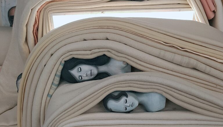 A stack of colorful blankets arranged neatly, with several mannequin heads placed on top, all set against a cozy indoor backdrop.