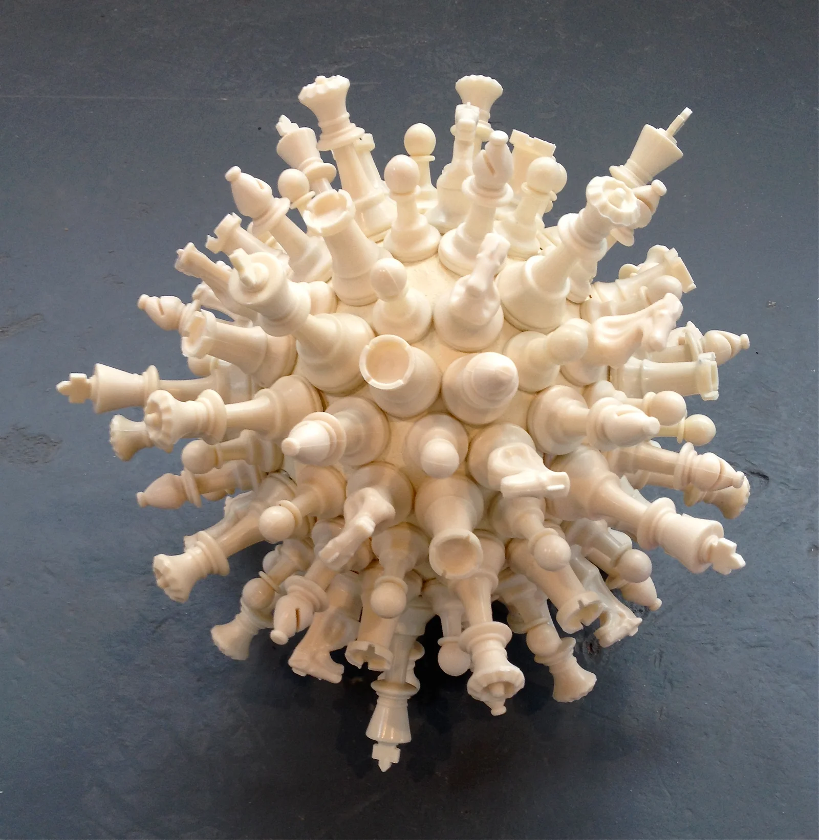 A spherical cluster of chess pieces, intricately arranged, creating a striking visual resembling a virus structure.
