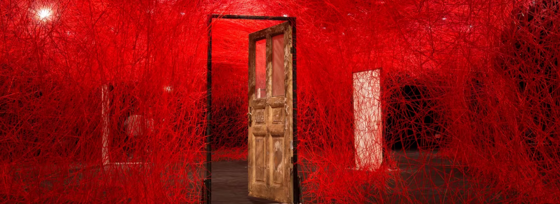 A weathered wooden door framed by vibrant red thread installations, creating an immersive art space.