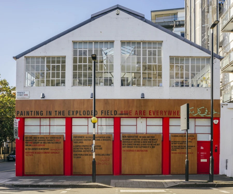 Exterior view of a gallery featuring a large wooden sign with text reading "Painting in the Exploded Field" and various artistic phrases.