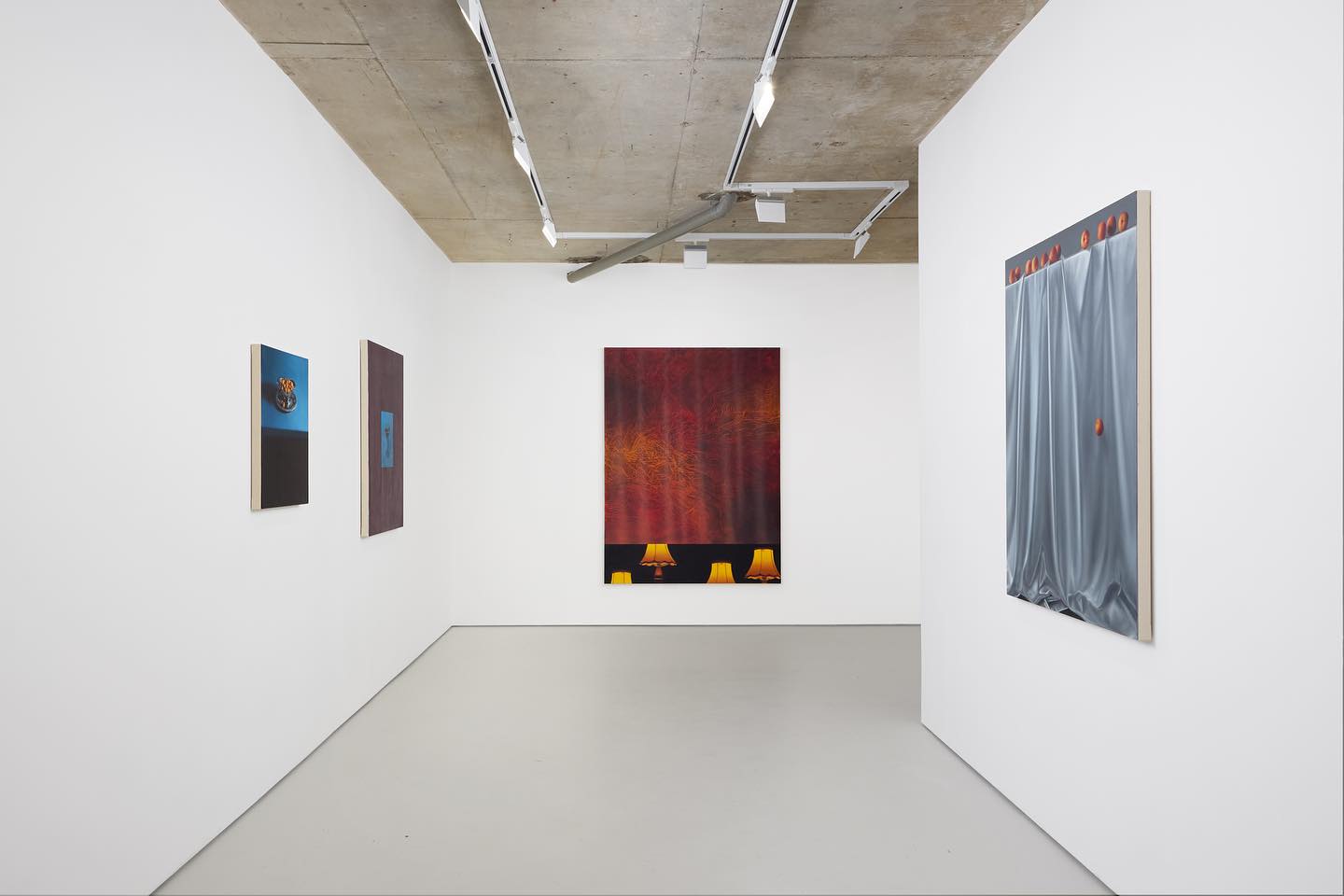 An art gallery with four paintings displayed on white walls, featuring abstract designs and a warm color palette. Modern lighting illuminates the space.