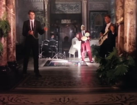 A group of people indoors playing various musical instruments, including a guitar, dressed in formal attire.