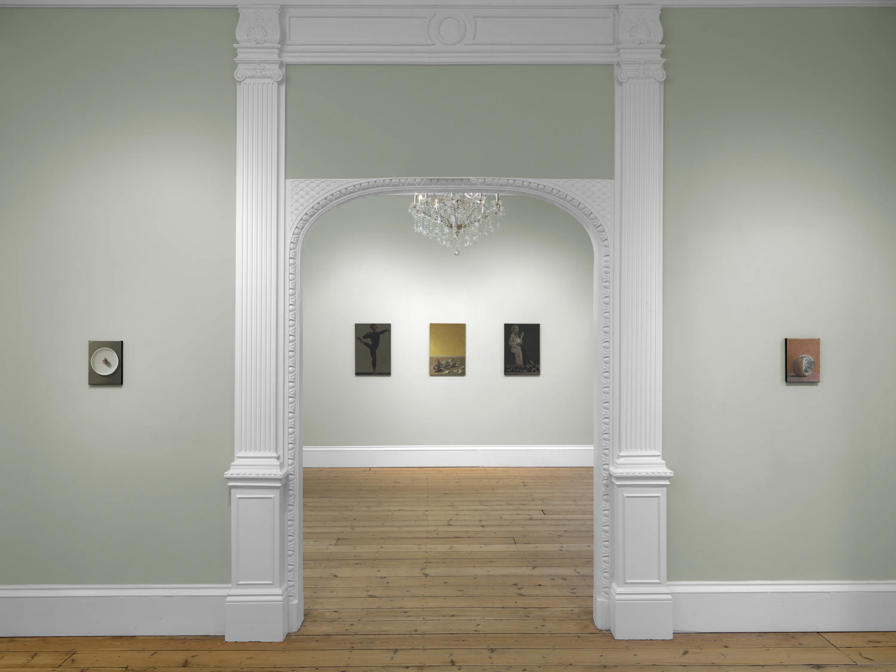 A room featuring white walls and white columns, with decorative molding and a ceiling. The floor is styled with a sleek design, and there's artwork displayed in picture frames along the walls.