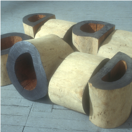 A collection of wooden objects arranged on a cement floor, featuring a pipe and ceramic items nearby.