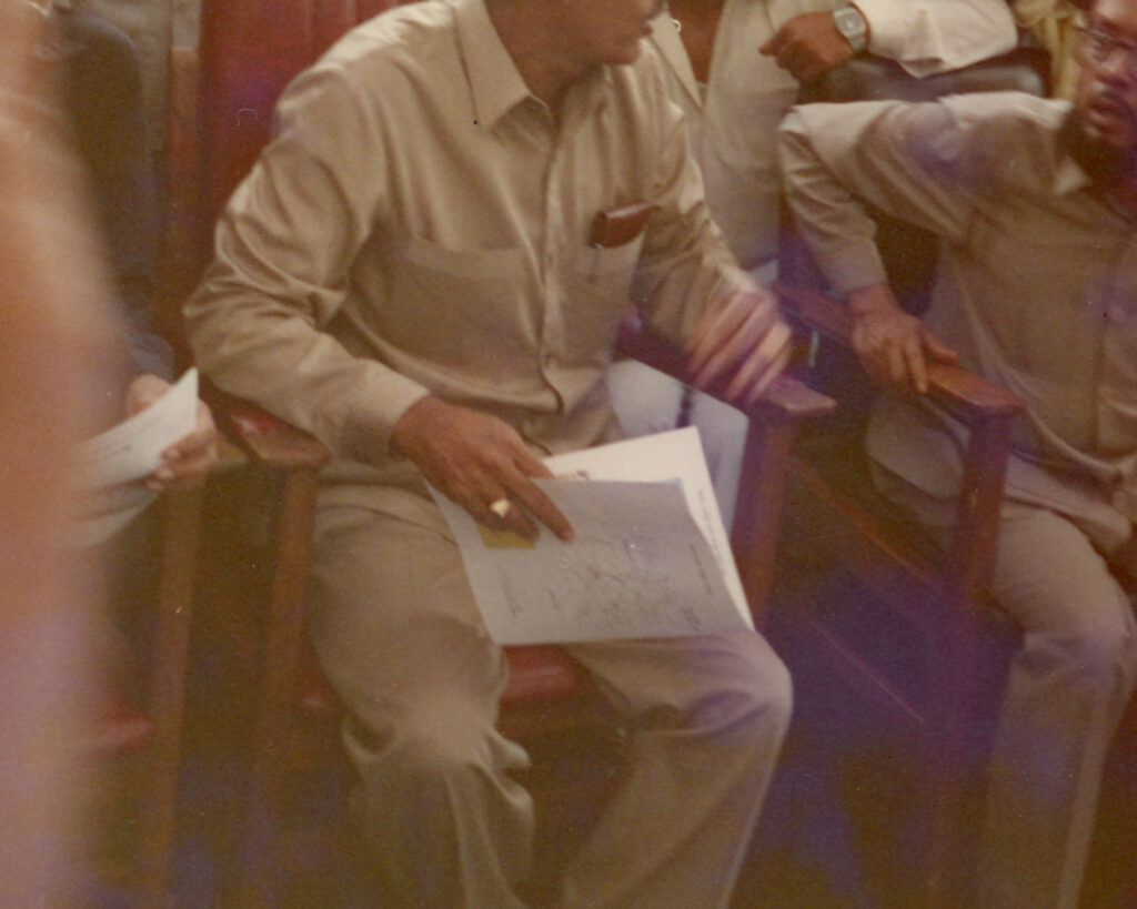 A group of people sitting in chairs indoors, some wearing martial arts uniforms.
