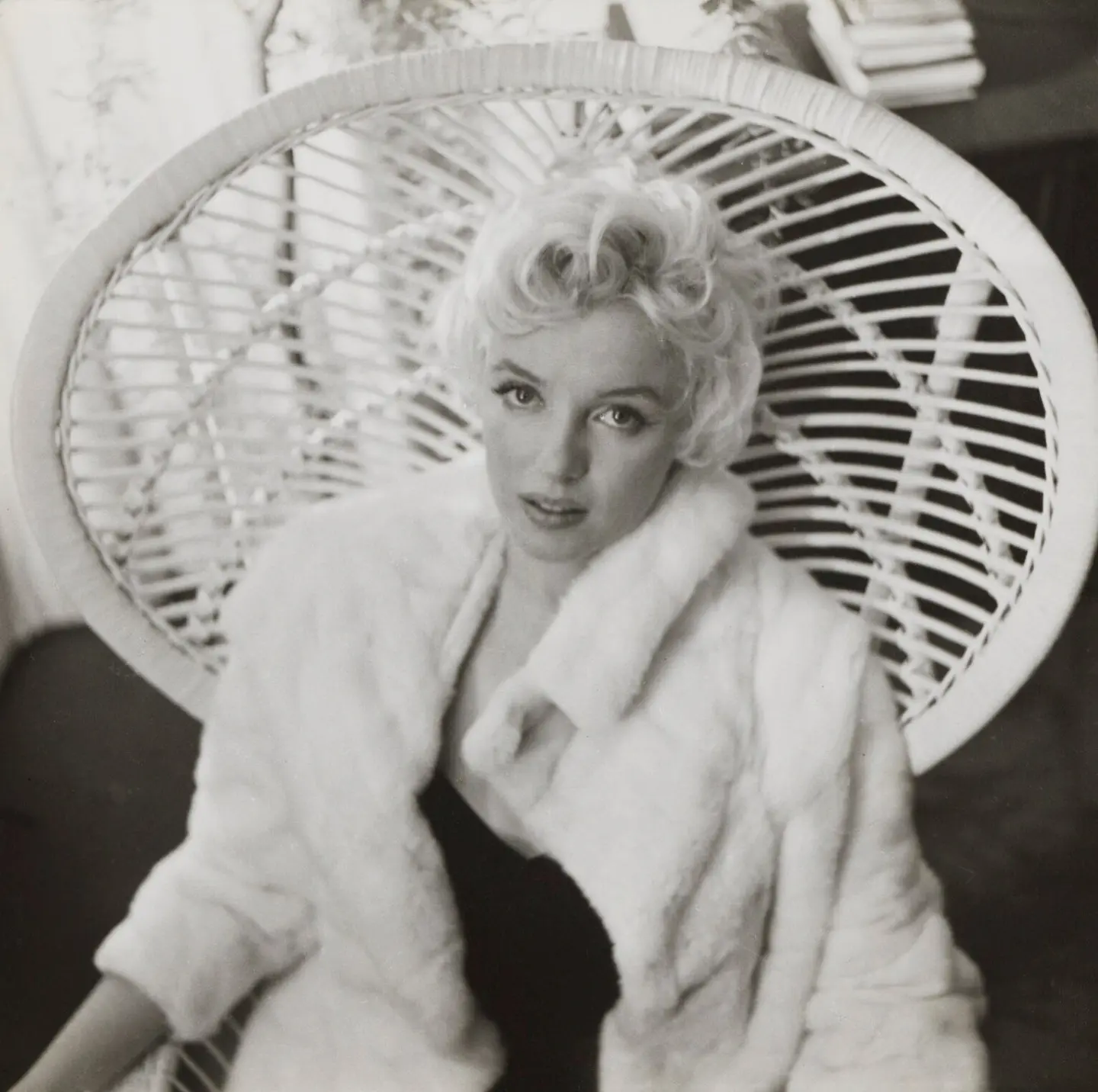 A woman in a white coat standing indoors next to a mechanical fan, depicted in black and white.