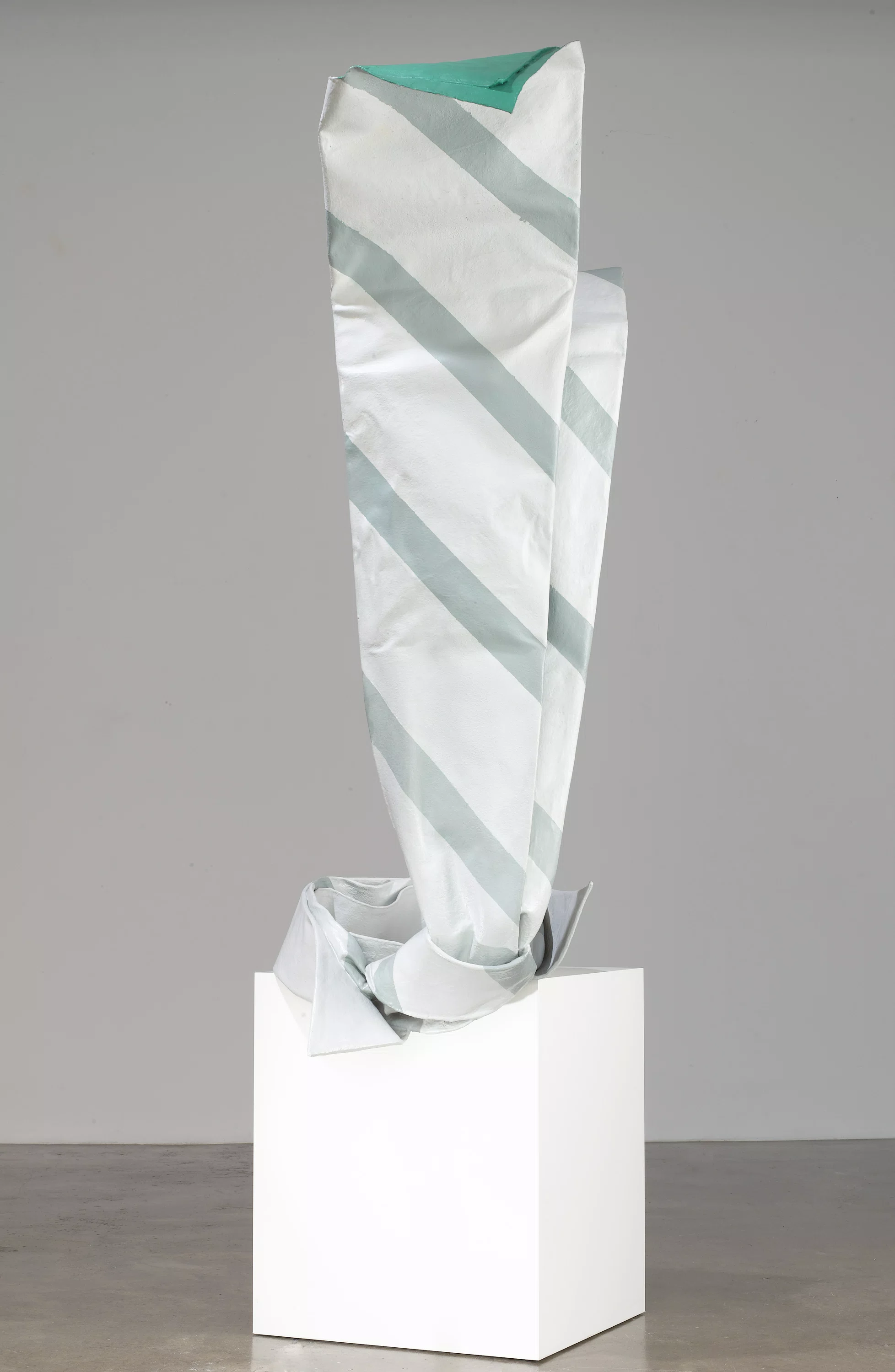 A white box containing a striped origami object, resembling a vase, arranged artistically.