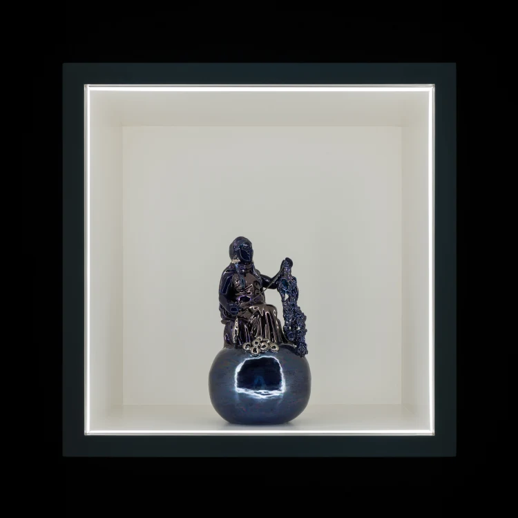 A statue displayed in a white box within an indoor museum setting, framed by the walls of the gallery.