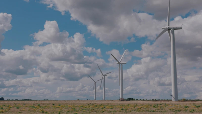 A group of wind turbines standing tall in a grassy field under a cloudy sky, showcasing renewable energy technology in an outdoor landscape.